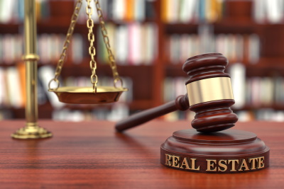 On a desk is a scale and a gavel. The gavel has the words Real Estate at the bottom - McGrath Law Firm - Real Estate Law - Mount Pleasant, SC