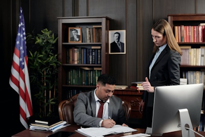 A woman is standing next to the desk, where a man is writing a note in a legal notebook, McGrath Law Firm, Wills, Mt. Pleasant, S.C.